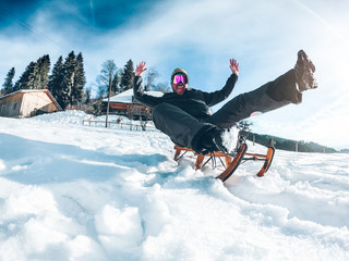 Young crazy man having fun with wood vintage sledding on snow mountain landscape