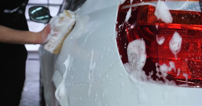 Professional guy (man) in a car wash washes a very dirty car using Karcher and splashes foam, wipes the car with a sponge. Concept of: Car wash, Wash accessories, Under high pressure.