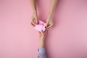 man gives a girl a gift from hand to hand, box wrapped in decorative paper on a pink pastel background, the concept of holidays, top view