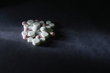 Fototapeta na wymiar remedies - medicine drug pills in white and pink color, several sizes, on black background and dramatic light - health, supplement, hypochondria concept