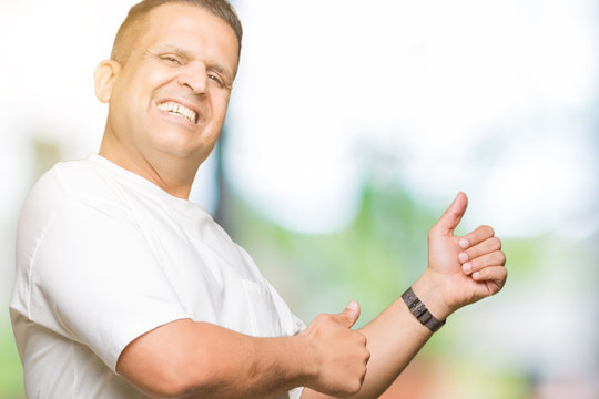 Middle age arab man wearig white t-shirt over isolated background Looking proud, smiling doing thumbs up gesture to the side