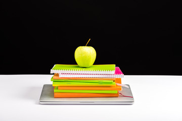 colorful notebooks, apple and laptop on desk isolated on black