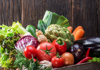 Fresh multi-colored vegetables in wooden crate. Wooden background.