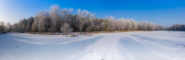 Rime and hoarfrost covering trees. Aerial view of the snow-covered forest and lake from above. Winter scenery. Landscape photo captured with drone.