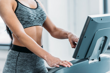 cropped shot of african american girl in sportswear training on treadmill in gym