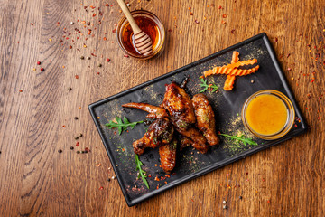 The concept of Indian cuisine. Baked chicken wings and legs in honey mustard sauce. Serving dishes in the restaurant on a black plate. Indian spices on a wooden table. background image.