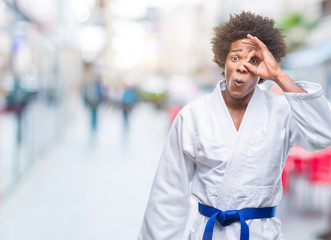 Obraz premium Afro american man wearing karate kimono over isolated background doing ok gesture shocked with surprised face, eye looking through fingers. Unbelieving expression.