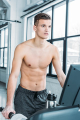 Obraz premium muscular shirtless man running on treadmill and looking away in gym