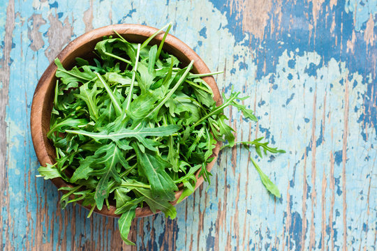Fresh leaves of arugula in a wooden bowl on a wooden table. Top view. Copy space