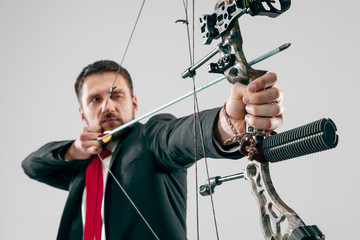 Businessman aiming at target with bow and arrow isolated on gray studio background. The business,...