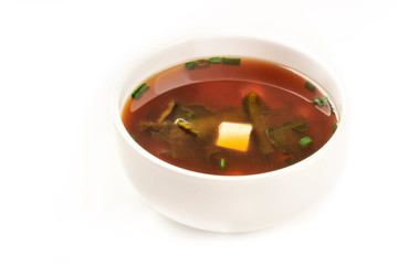 A photo of a bowl of miso soup with tofu, scallions, and wakame algae, on a white background with copy space
