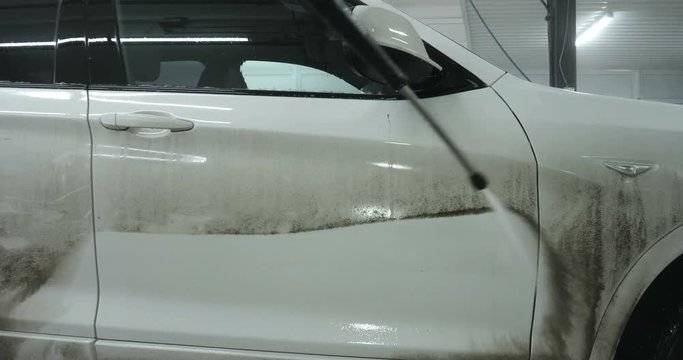 Professional guy (man) in a car wash washes a very dirty car using Karcher and splashes foam, wipes the car with a sponge. Concept of: Car wash, Wash accessories, Under high pressure.