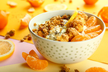 Tasty granola with yogurt and fruits in bowl on color background