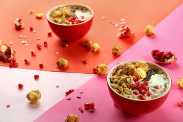 Tasty granola with yogurt and pomegranate seeds in bowl on color background