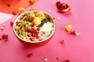 Tasty granola with yogurt and pomegranate seeds in bowl on color background