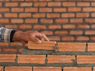 Worker in orange put hand on brown brick and mortar cement brick