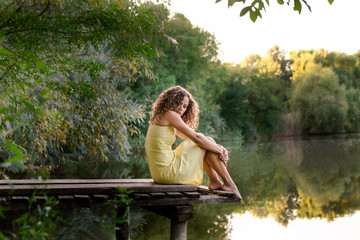 Young woman sitting on wooden pier near lake.