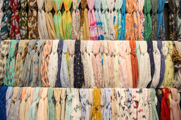 Many bright female scarfs and shawl. colorful scarves hanging in the market. clothes rack with a selection of scarves or scarfs.  pattern of many scarves colorful vibrant colors, hanging, on display.