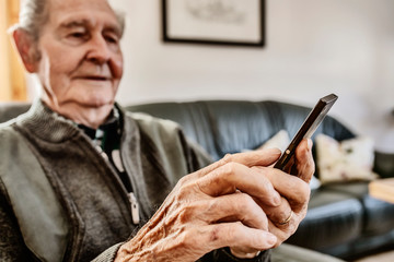 Senior surft zuhause mit seinem smart phone im Internet