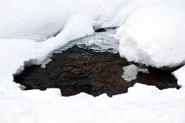 Stream in winter forest. Large drifts of snow. Spring thaw.
