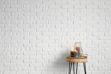 Burning candles on wooden table near white brick wall