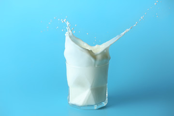 Glass of tasty milk with splashes on color background