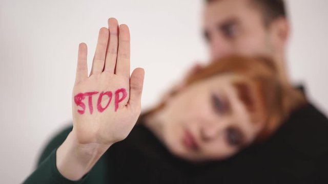 Silhouette of couple in white background, man cuddle woman and stroke her head, female showing written sign at her hand "stop" violance
