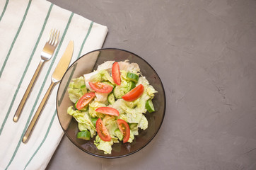 healthy salad, vegetable, tomatoes, cucumbers, iceberg, Cutlery, kitchen towel, grey background. Copy space. Vegetarian