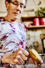 Seniorin schält eine Kartoffel in der Küche