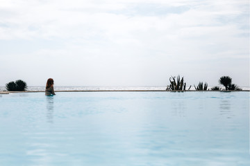 Obraz na płótnie Canvas Young redhead woman in an infinity pool near the ocean