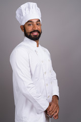 Portrait of young handsome Indian man chef smiling
