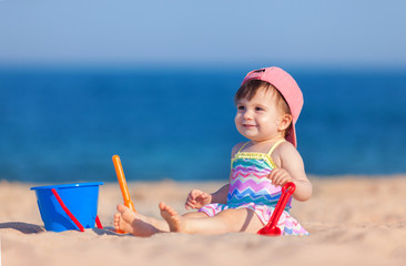 Happy childhood, happy family vacation. Cute child on the sea background. Happy little girl playing with sand on the beach of sea. Summer vacation. Summer lifestyle