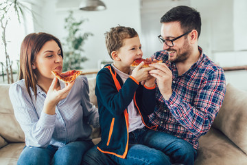 Portrait of happy family eating pizza while sitting on sofa at home