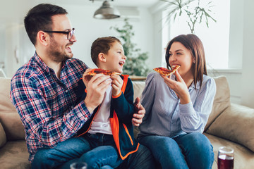 Portrait of happy family eating pizza while sitting on sofa at home
