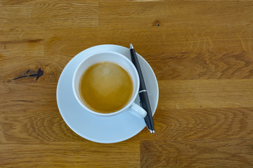 Tasse Kaffee auf Holztisch am Arbeitsplatz Homeoffice mit Kugelschreiber 