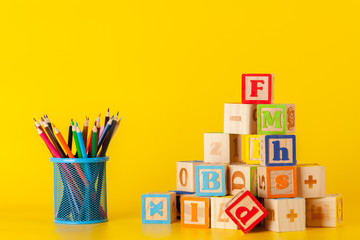 Colorful wooden blocks and cup with colorful pencils on a yellow background