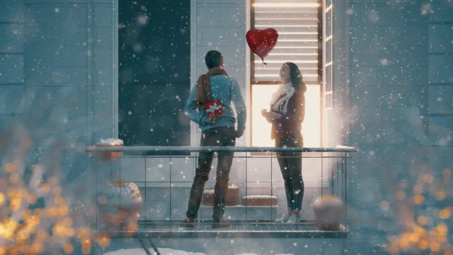 Romantic couple holding Valentines gift standing on the balcony on a date.