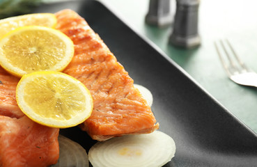 Pieces of tasty grilled salmon with lemon and onion on plate, closeup