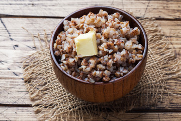 Boiled buckwheat with a piece of butter in a wooden bowl on a rustic table.