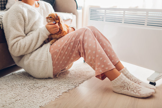 Using Heater At Home In Winter. Woman Warming Body With Cat. Heating Season.