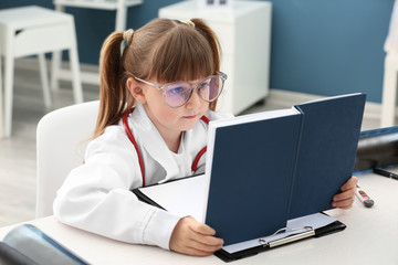 Cute little girl dressed as doctor playing at home