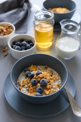 Granola bowl (oatmeal porridge) with blueberry, honey and milk on gray table. Flat lay. Selective focus. Healthy vegetarian food