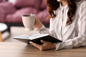 Obraz premium Beautiful young woman drinking coffee while reading book at home