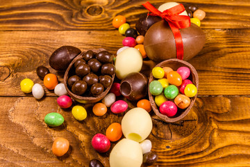 Chocolate easter eggs and multicolored candies on wooden table. Top view