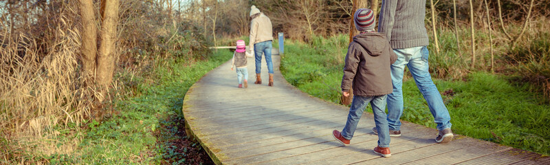 Back view of family walking together holding hands over a wooden pathway into the forest