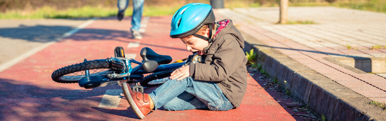 Boy in the street ground with a knee injury screaming after falling off to his bicycle