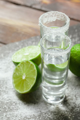 Tequila silver shots with lime slices and salt on wooden board