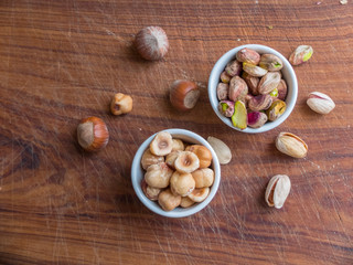 Top view of two ceramic cups containing toasted and peeled hazelnuts and one of pistachios.