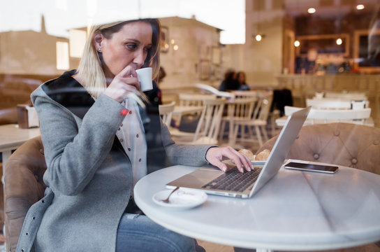 Outside view through a glass of young business woman taking a coffee and working in her laptop
