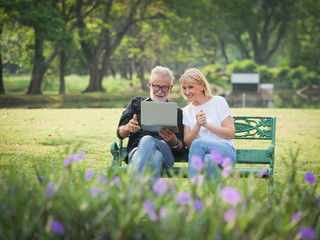 Two happy seniors retirement Man and woman are sitting and using computer laptop in park